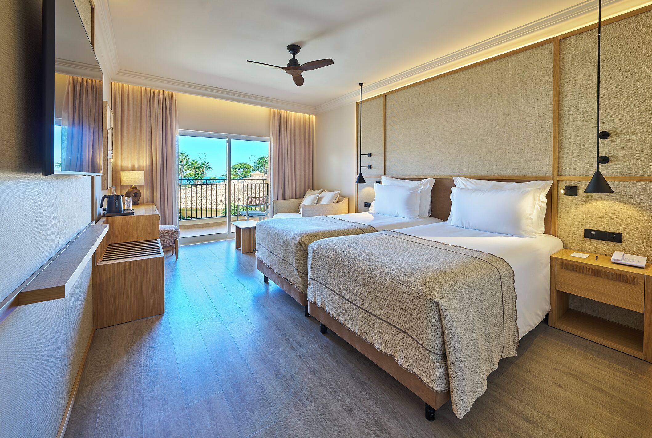 A hotel room with a bed, bedside tables, a desk, a chair, a balcony view, and a ceiling fan.
