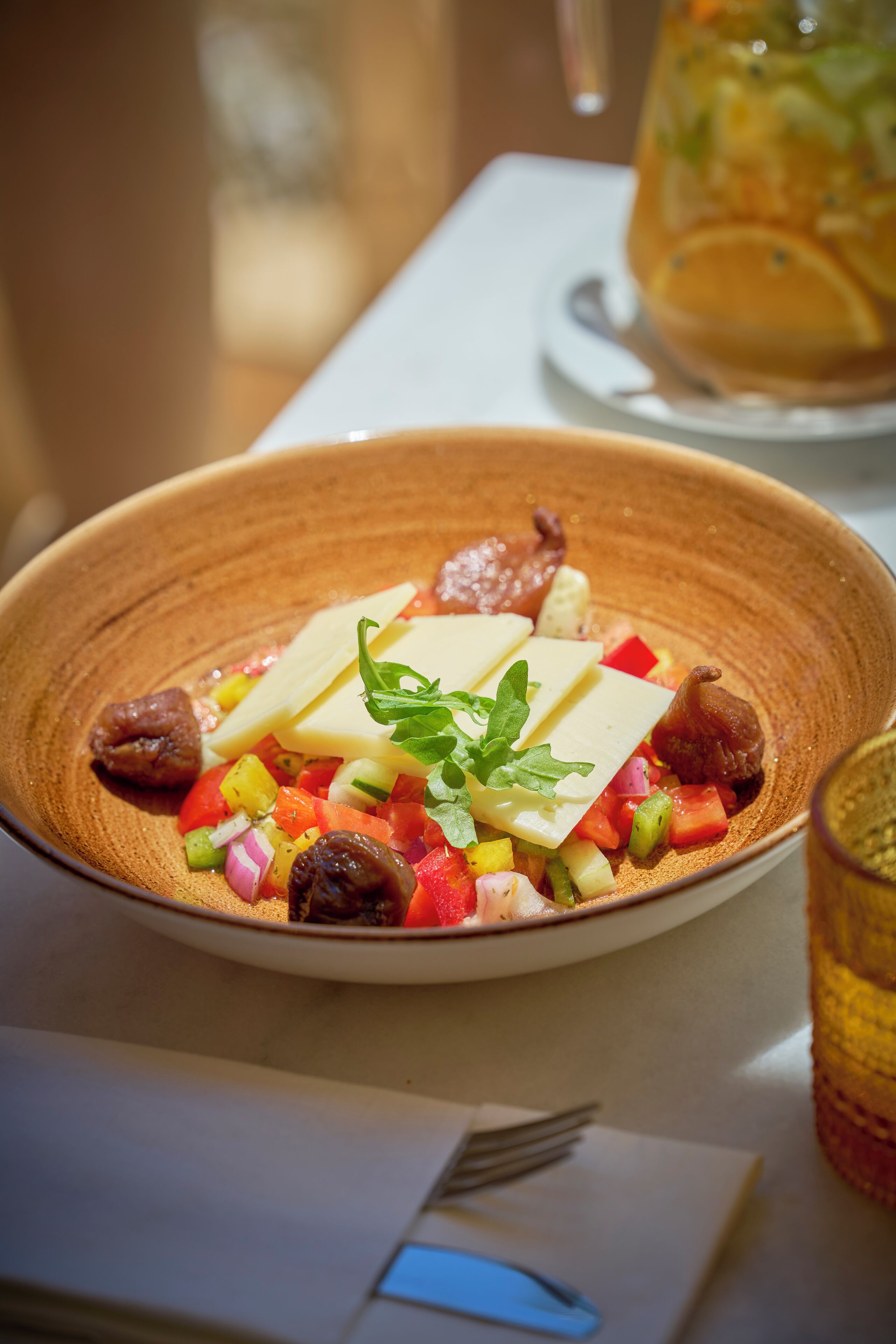 A bowl of salad with cheese and nuts, a glass of drink, and a fork on a table.