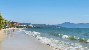 Una playa con vista despejada al océano, una montaña a lo lejos y edificios a lo largo de la costa.