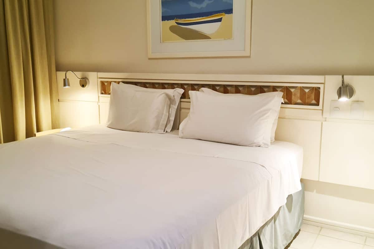 A neatly made bed with white linens, a headboard with a geometric pattern, and a framed picture of a boat on the wall.