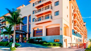 Un hotel de varios pisos con un llamativo letrero que dice 'Juré Beach Village', con balcones y una entrada ajardinada.