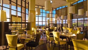 Un restaurante con sillas y mesas amarillas, ventanas amplias y lámparas colgantes.