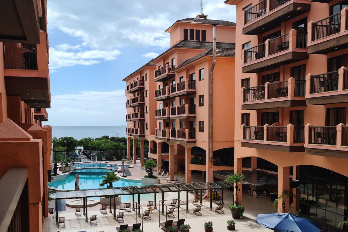A hotel courtyard with a swimming pool, outdoor seating, and multiple balconies.