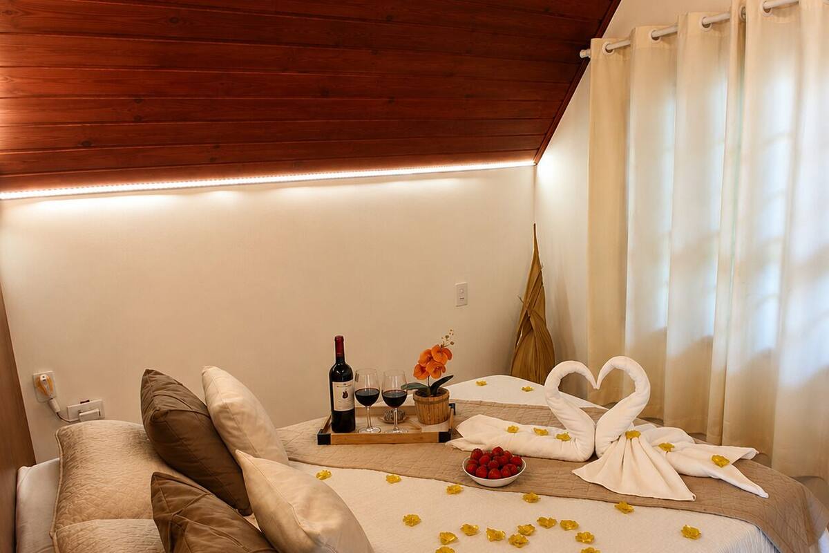 A cozy room with a bed, pillows, a tray with a bottle, glasses, and flowers.