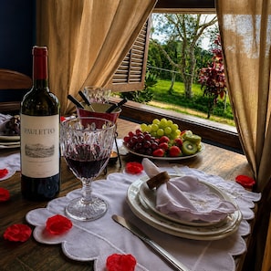 Mesa posta com uma garrafa de vinho Pauletto, um copo de vinho tinto, uma tigela de uvas e morangos e um prato de kiwi.