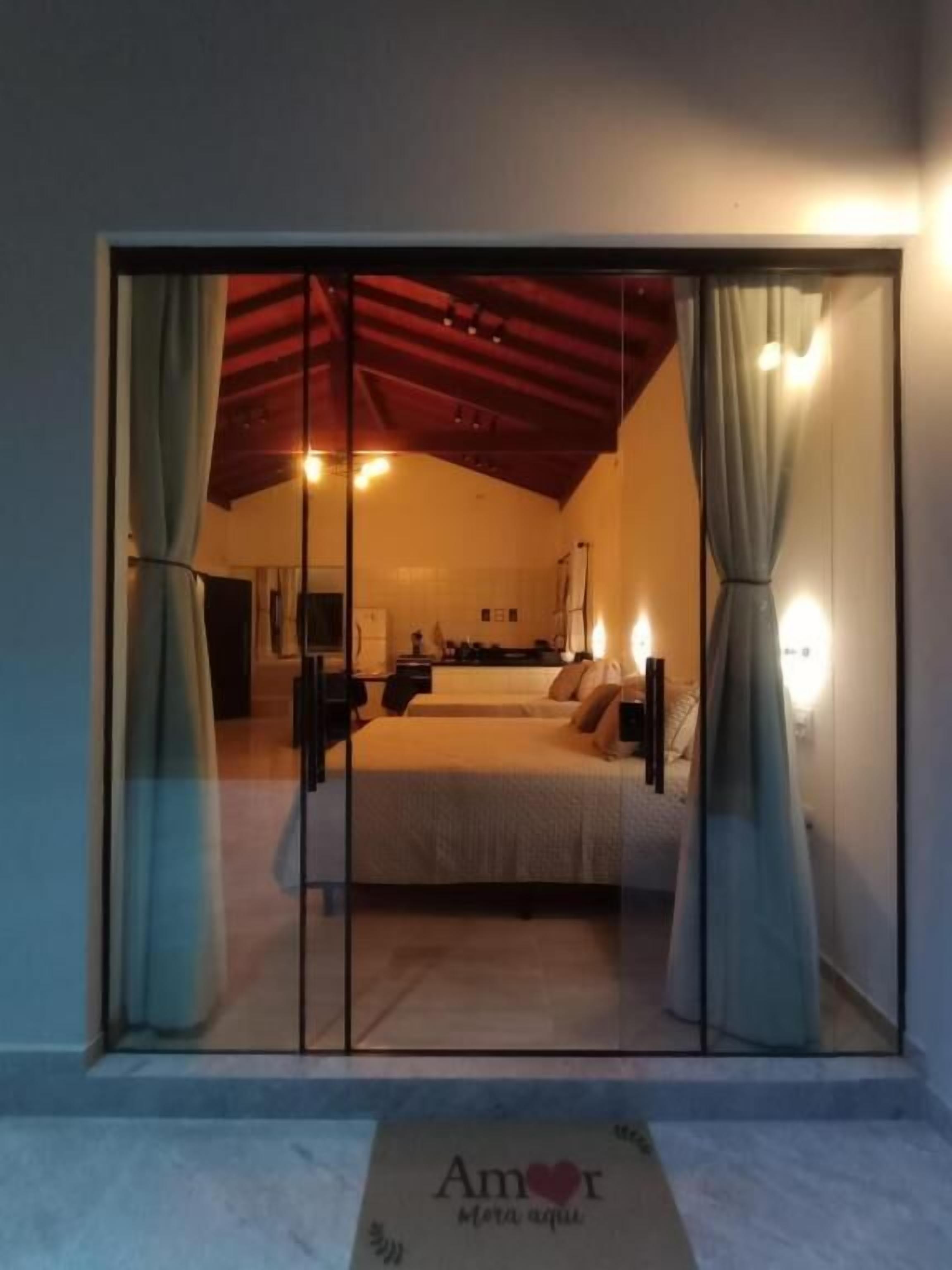 Quarto com cama, cortinas e porta de vidro deslizante para uma varanda.