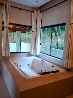 Un baño moderno con una bañera grande, ventanas amplias y cortinas.
