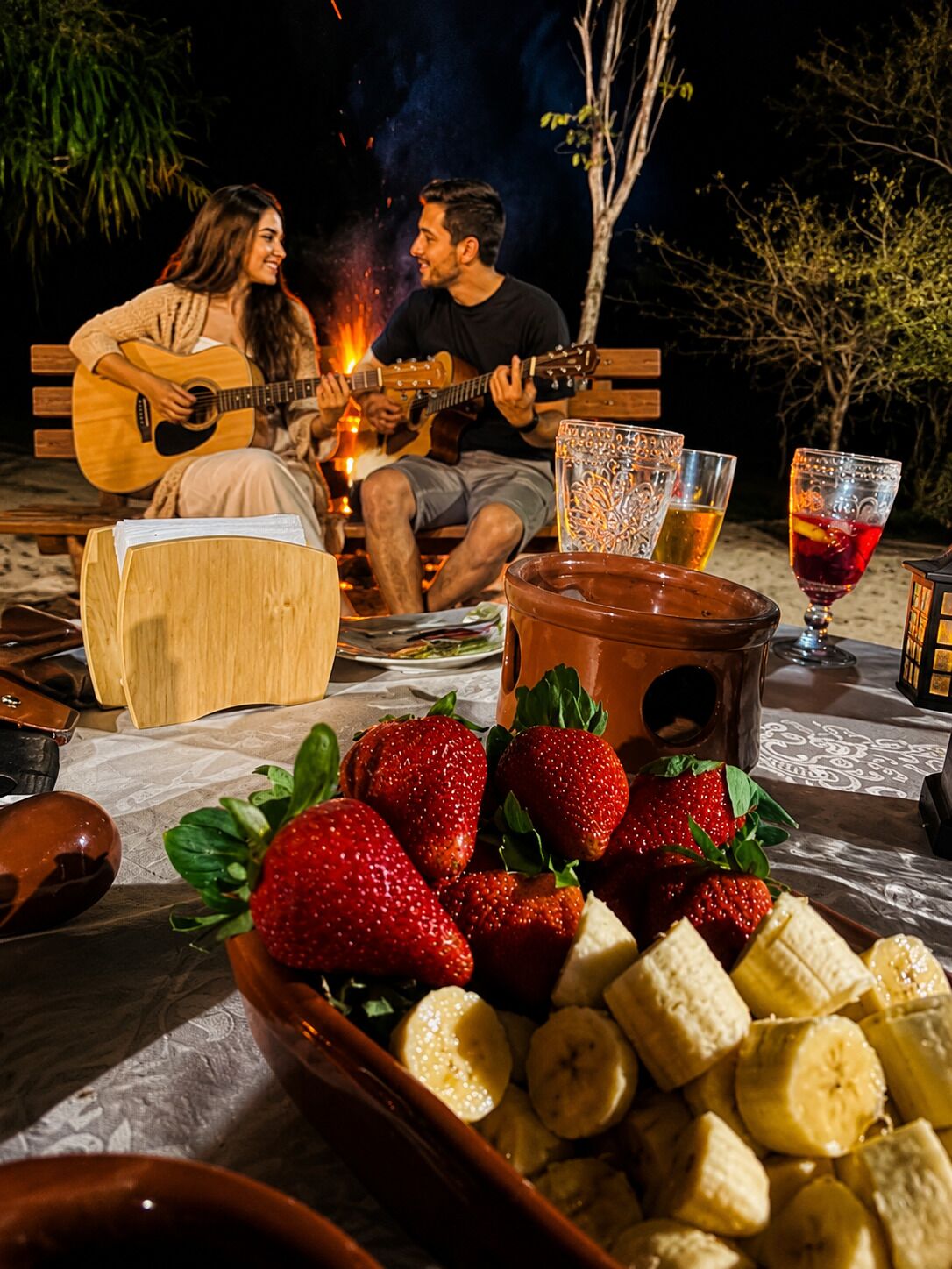 Een gezellige buitenomgeving met een vuurkorf, een gitaar en een tafel vol eten en drinken.