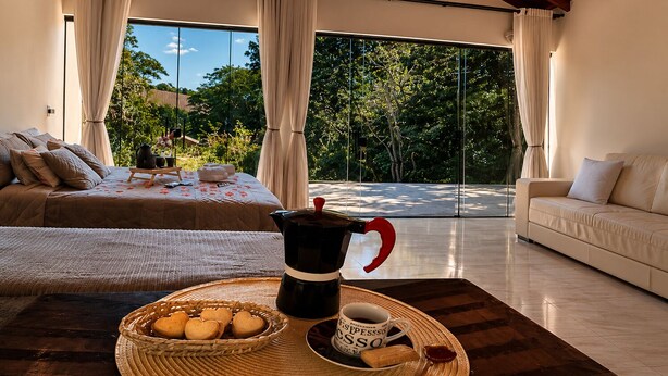 Un dormitorio moderno con una cama, una mesita de centro con pasteles, una cafetera y una taza.