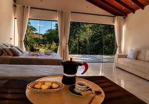 Quarto moderno com uma cama, uma mesa de centro com doces, uma cafeteira e uma xícara.