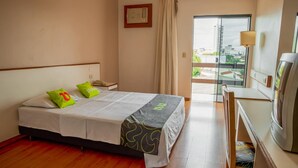 Ein Hotelzimmer mit Bett, Schreibtisch, Stuhl, Lampe und Blick auf die Stadt durch das Fenster.