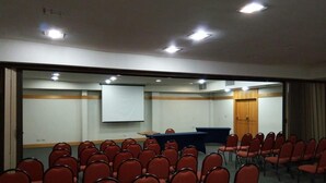 Ein Konferenzraum mit Reihen roter Stühle, einer Tafel und einer Projektionsleinwand.