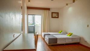 Ein Hotelzimmer mit Holzboden, zwei Einzelbetten mit grünen Kissen, einem kleinen Tisch und einem Fenster mit Vorhängen.