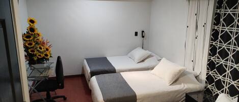 A hotel room with two beds, a desk with a chair, and a vase of sunflowers.