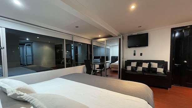 A modern hotel room with a large bed, a seating area with a table and chairs, a sofa, and a flat-screen TV mounted on the wall. - Hotel Ejecutivo Embajada (Bogotá)