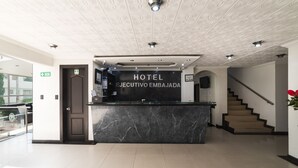A hotel reception area with a marble counter, a sign reading "HOTEL EXECUTIVO EMBAJADA," and a staircase leading to an upper floor. - Hotel Ejecutivo Embajada (Bogotá)