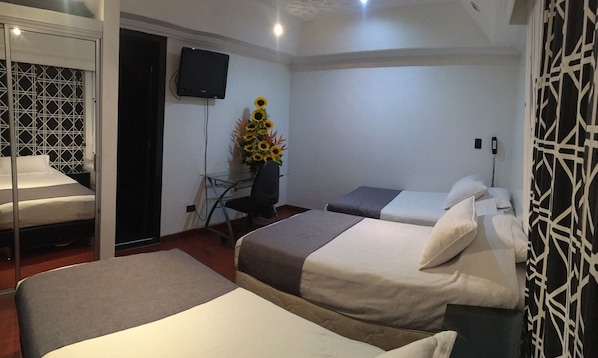 Habitación de hotel con dos camas, un escritorio, una silla, un televisor y un jarrón con girasoles.