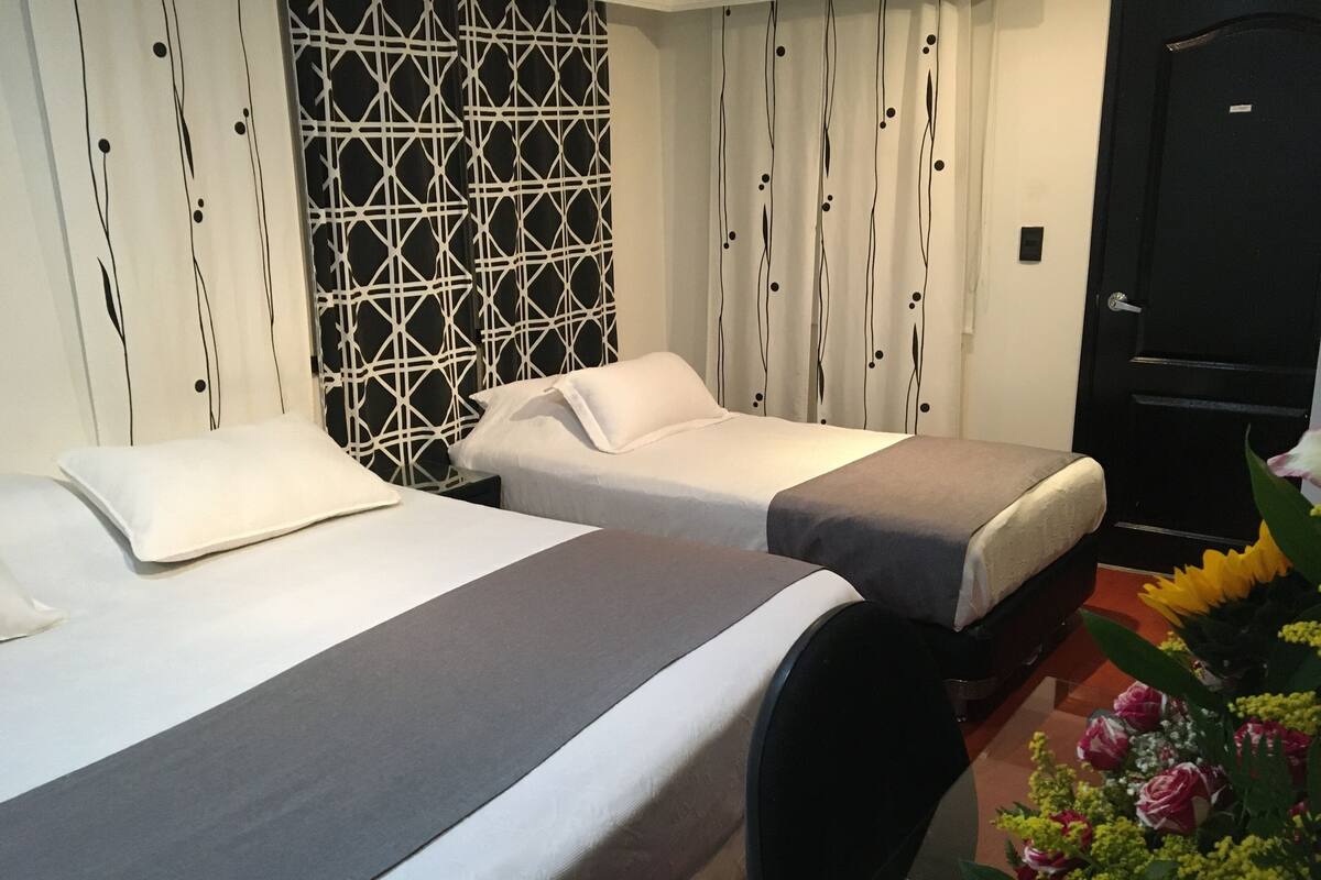 A hotel room with two beds, a black chair, a decorative wall, and a door.