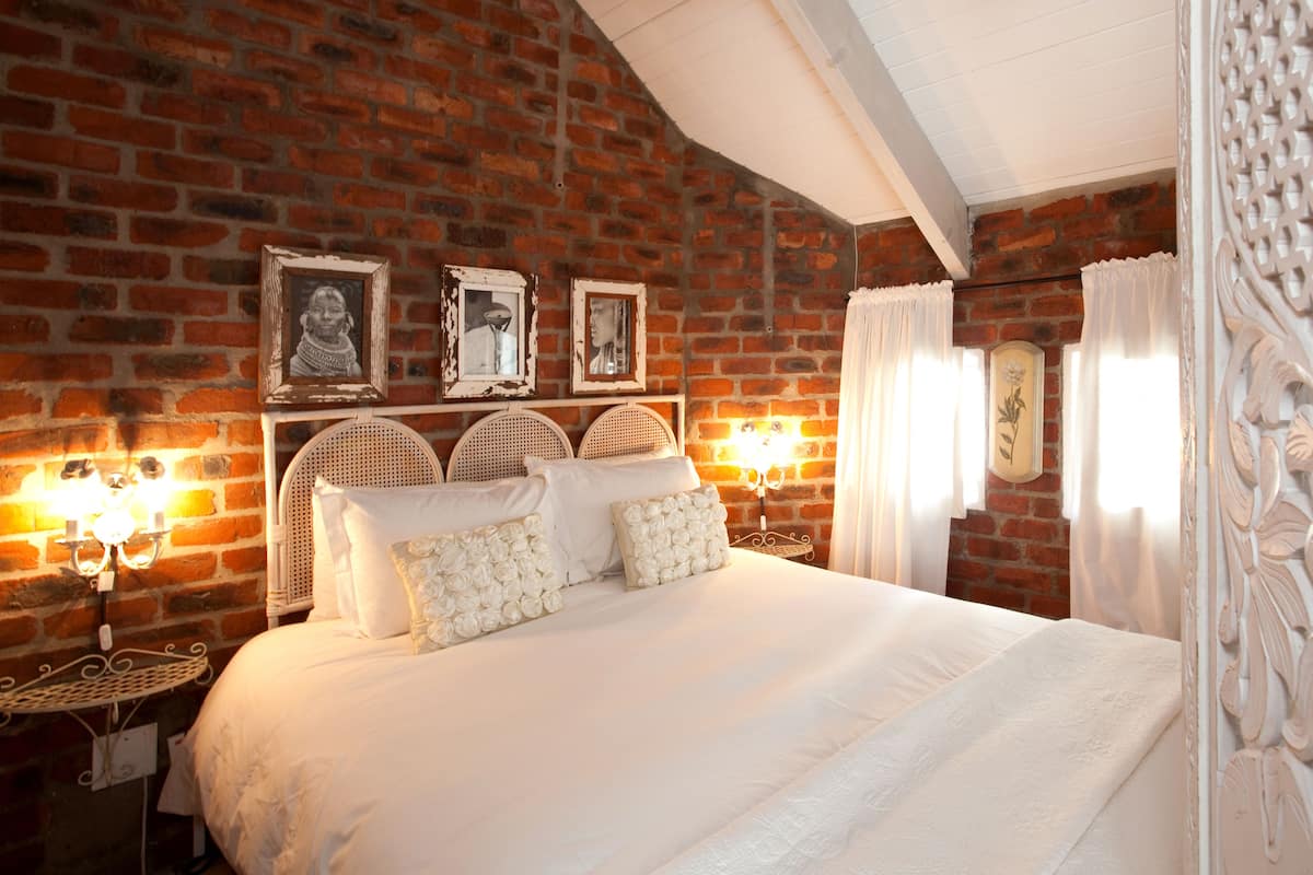 Un dormitorio con pared de ladrillo, cama blanca y cuadros en la pared.