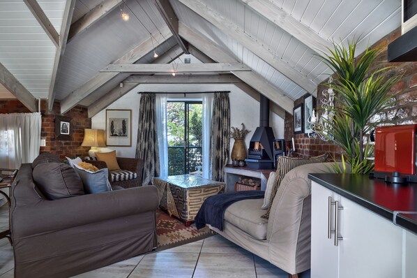 Acogedor espacio tipo loft con techo alto, vigas a la vista y chimenea. Cuenta con una zona de estar confortable con sofá y una mesa de comedor.