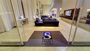 Una moderna hall d'albergo con reception, area salotto e un grande schermo che mostra un video.