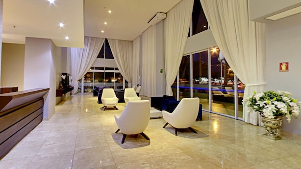 Una hall moderna con pavimento in marmo, poltrone bianche, una reception e un'ampia finestra con tende.