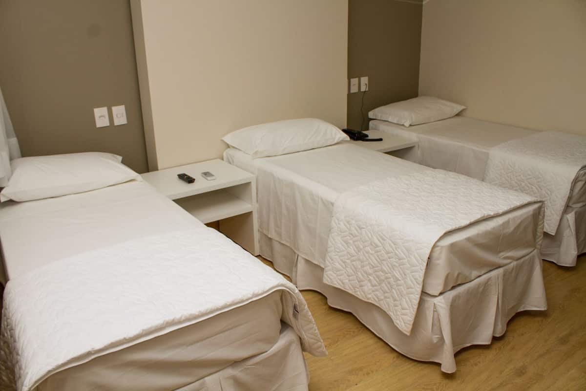 A hotel room with three single beds, a small bedside table with a phone and remote, and a wall socket.