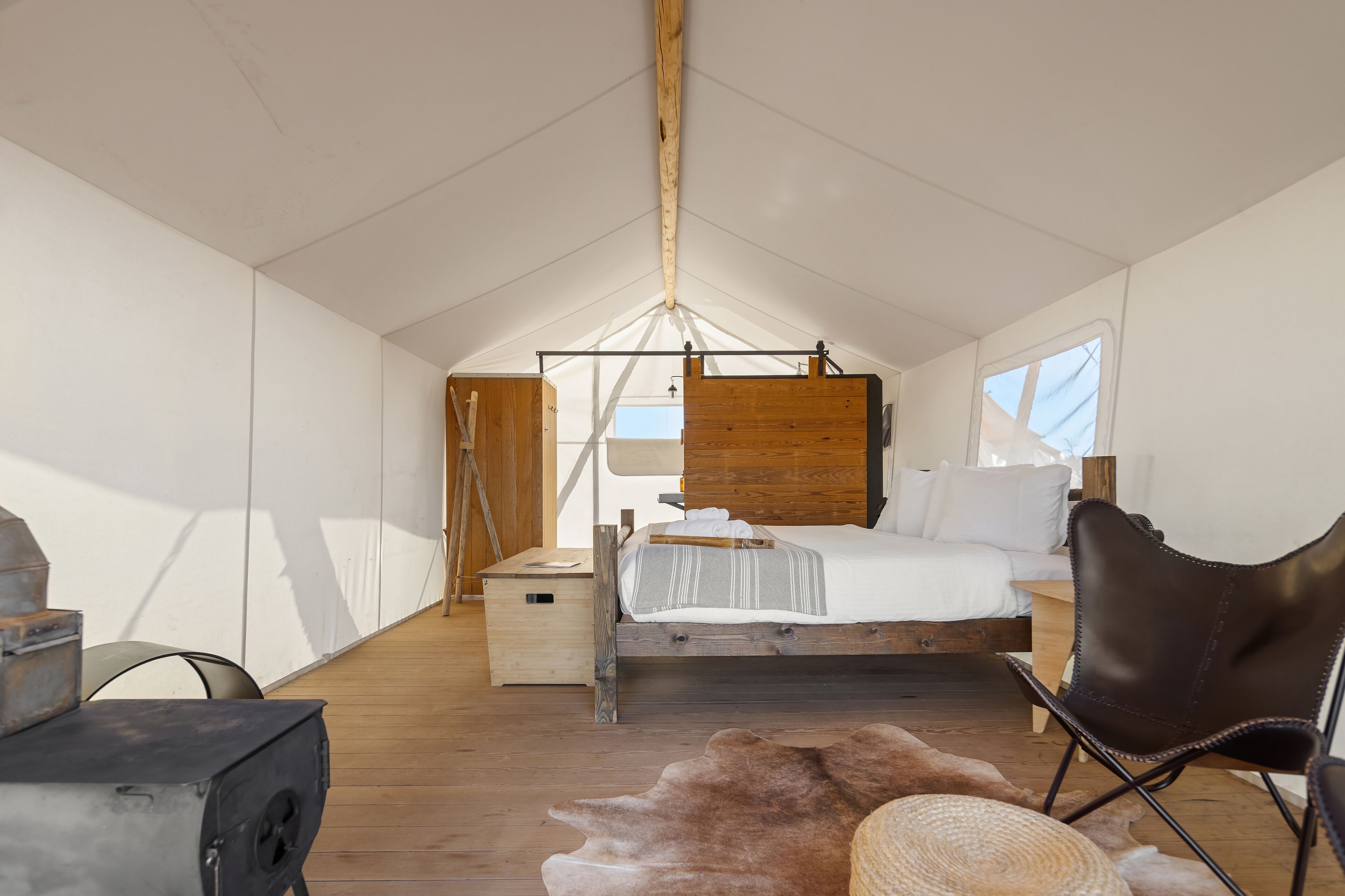 Una habitación con techos altos, una cama de madera, una mesita de madera y una alfombra de piel.