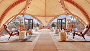 Un intérieur spacieux, aménagé comme une tente, avec un espace salon central, de nombreux fauteuils et des plantes en pot.