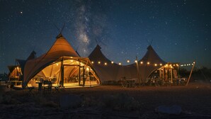 Une série de tentes en forme de dôme, décorées de guirlandes lumineuses, installées dans un environnement désertique, de nuit.