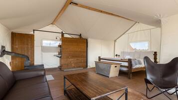 A tented accommodation with a wooden table, leather sofa, and a bed with a wooden frame.