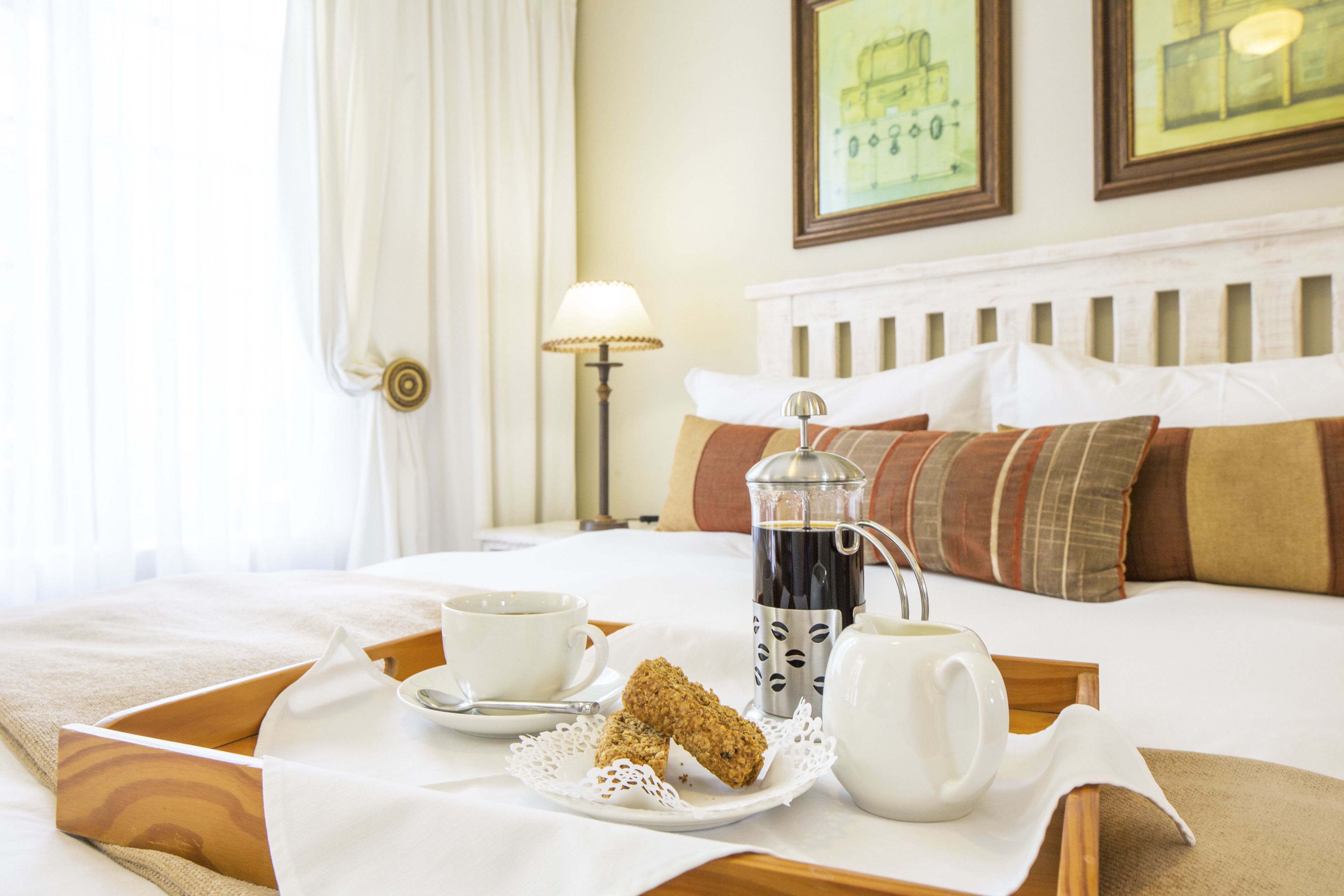 A neatly made bed with a tray of breakfast items including a cup of coffee, a teapot, a teacup, and a pastry.