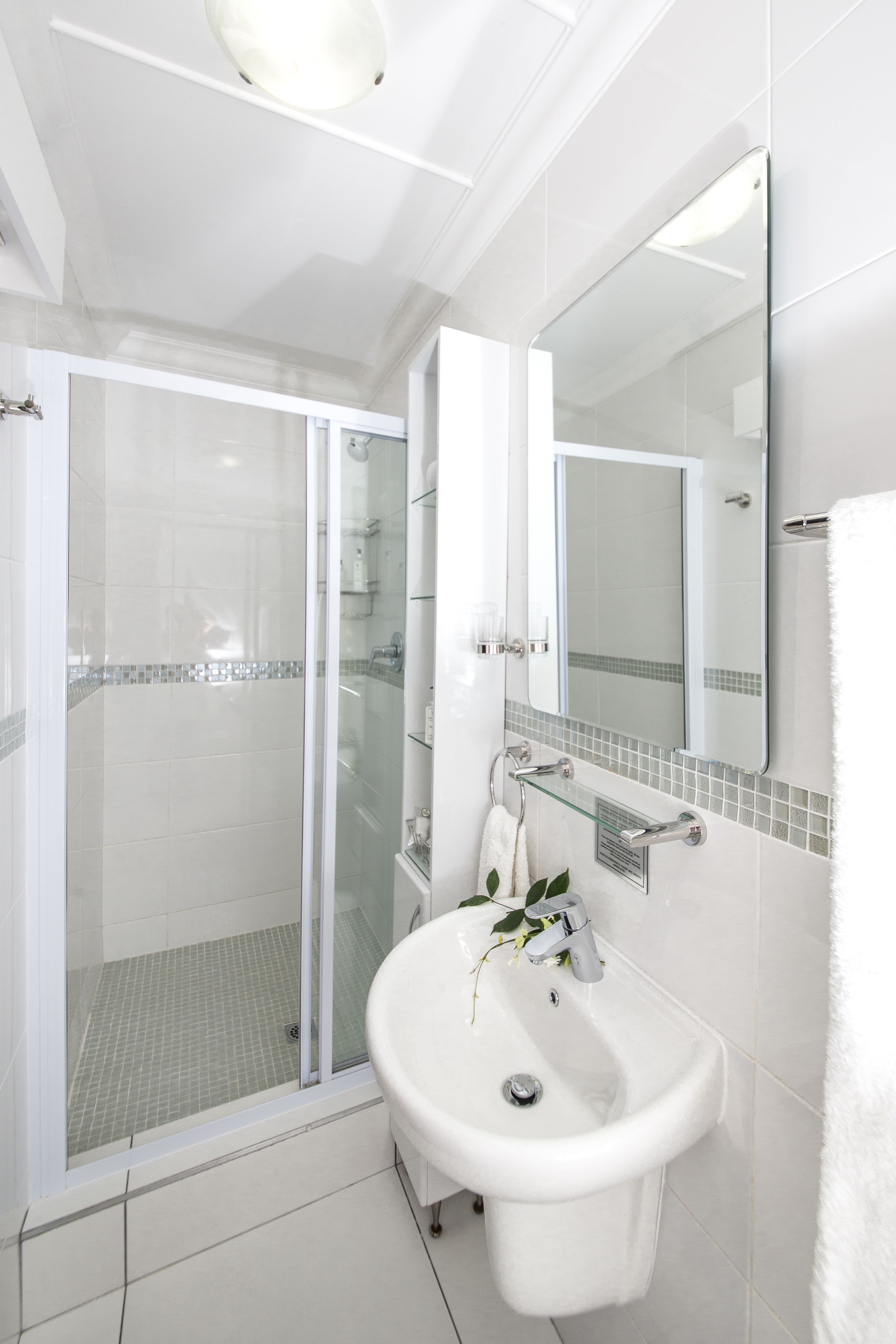 A modern bathroom with a glass-enclosed shower, a white sink, and a large mirror.