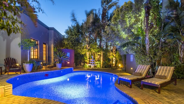 A swimming pool with a tiled edge, surrounded by lounge chairs and potted plants.