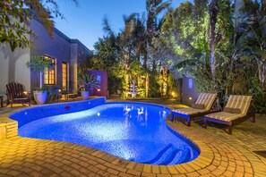 A swimming pool with a tiled edge, surrounded by lounge chairs and potted plants. - Kingfisher GuestHouse (Gqeberha (Port Elizabeth))