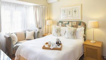 A hotel room with a bed, a bedside table, a nightstand, a window with curtains, and a tray with breakfast items.