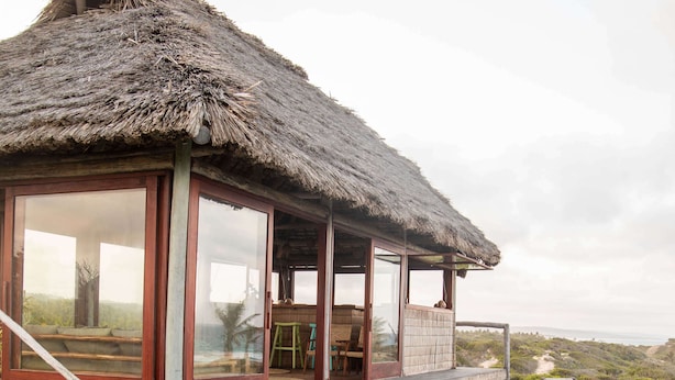A poolside area with a thatched-roof structure, wooden deck, and lounge chairs.