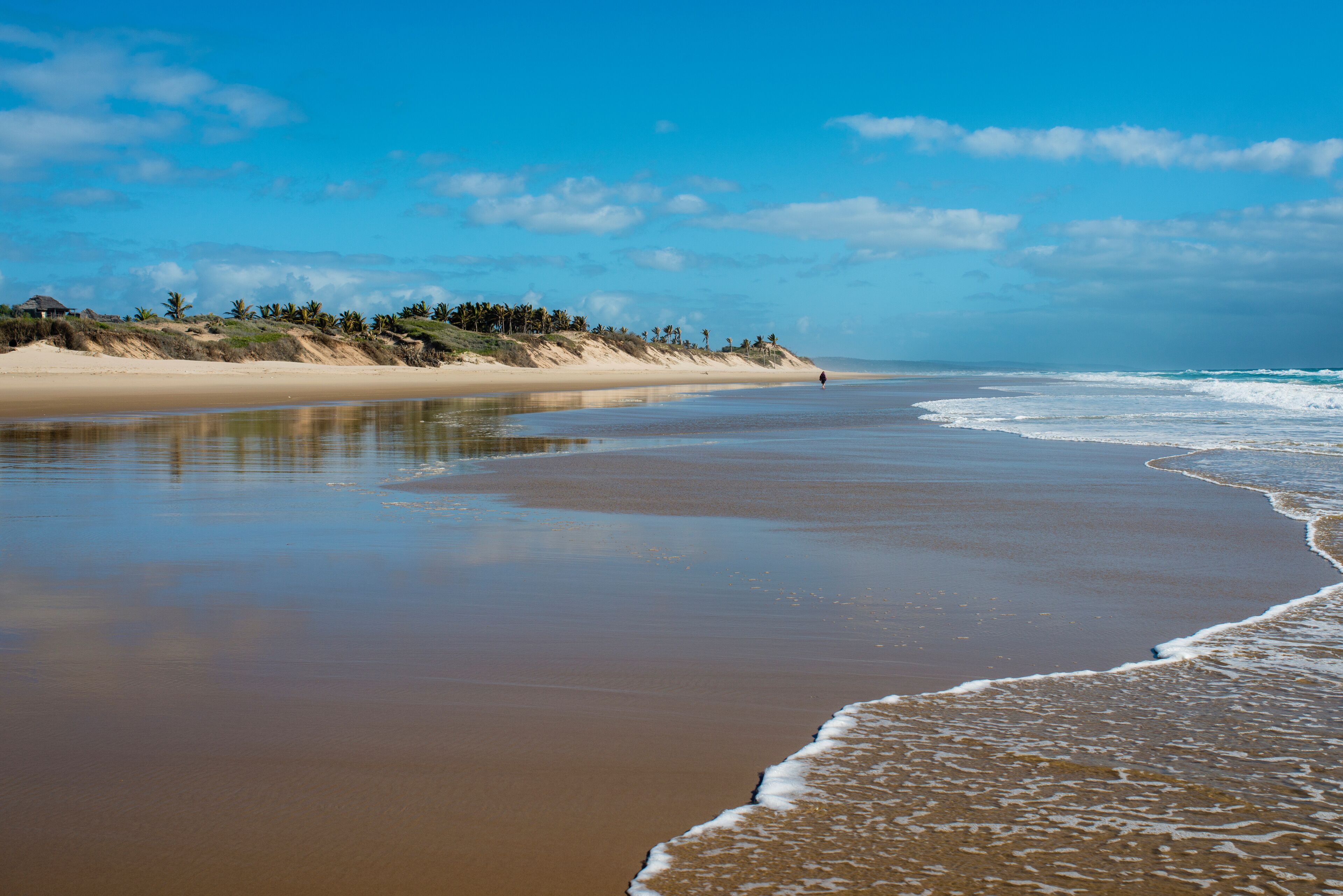 A beach with a sandy shore, calm waves, and a clear sky.