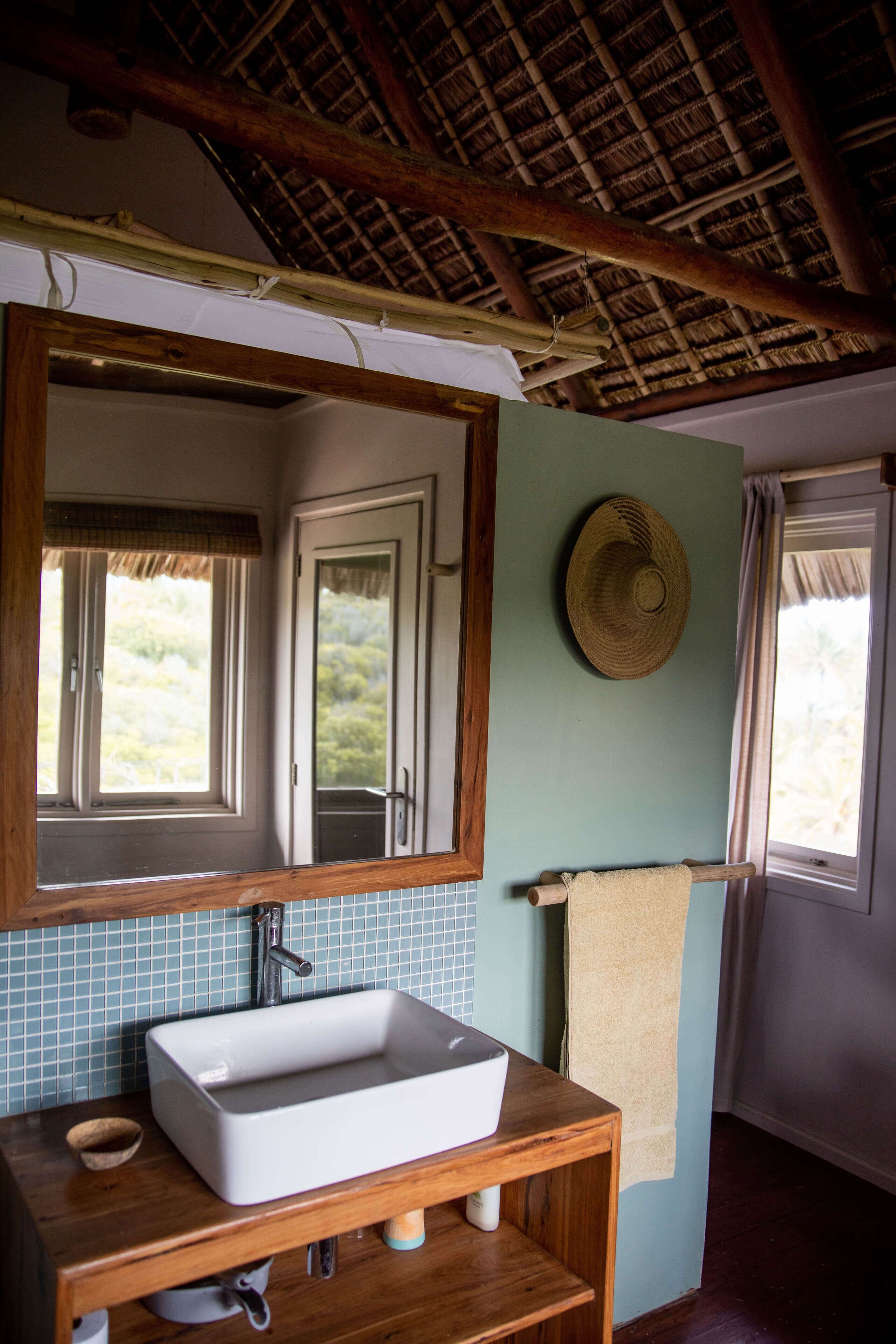 A bathroom with a wooden vanity, a white sink, a mirror, a towel rack, and a window with a view of greenery.