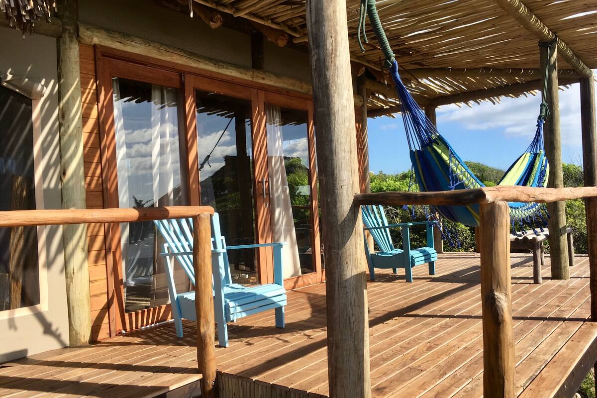 A wooden deck with a thatched roof, blue chairs, and a hammock.