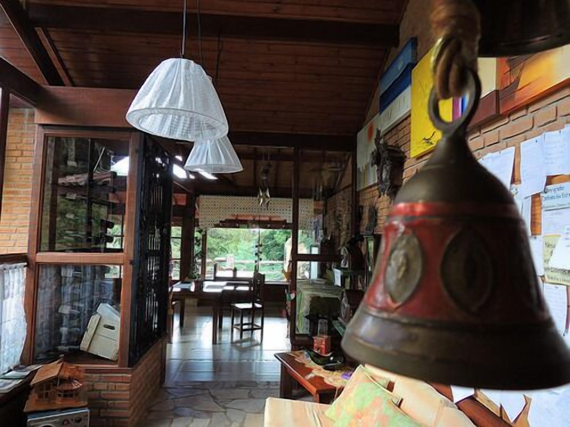 A rustic interior with a wooden ceiling, a bell, and a window overlooking greenery.
