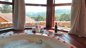 A room with a large bathtub filled with bubbles, a bottle, and glasses on a wooden table. - Pousada Cantinho das Estrelas (Camanducaia)