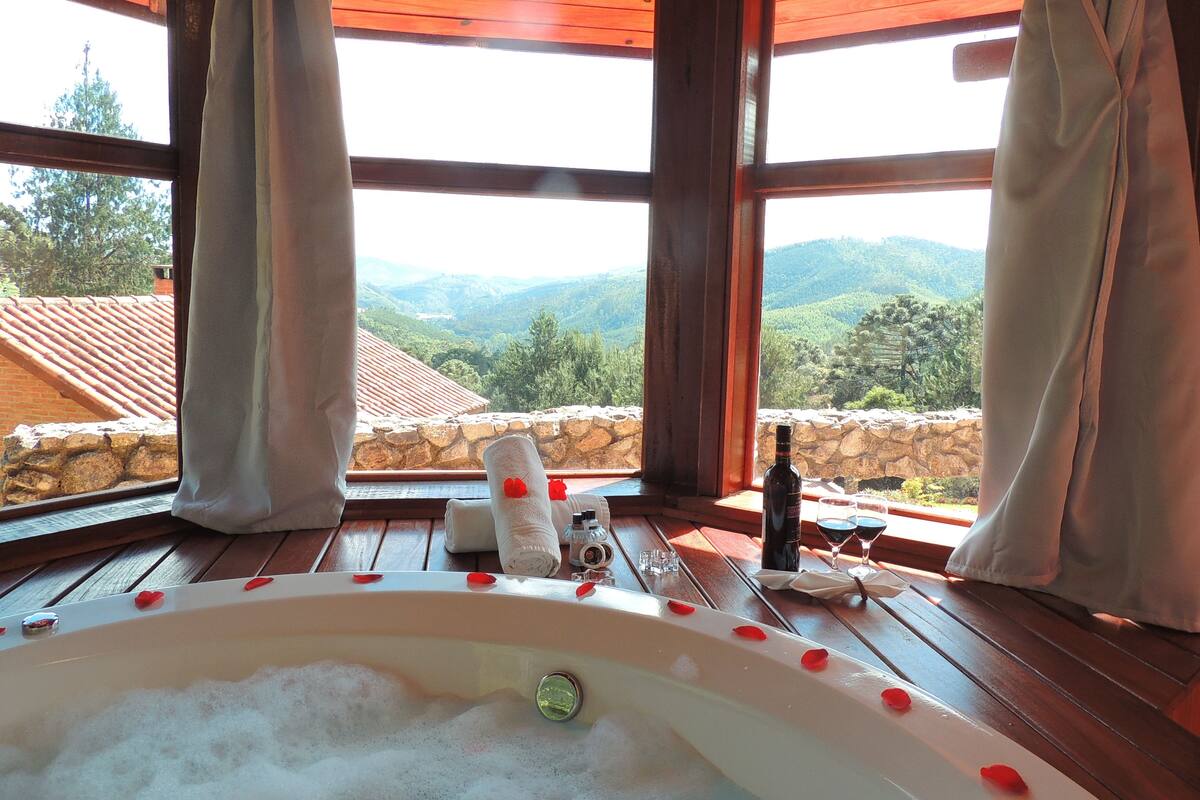 Ein Zimmer mit einer großen Badewanne, die mit Schaum gefüllt ist, einer Flasche und Gläsern auf einem Holztisch.