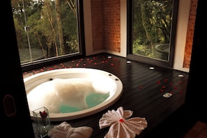 Un cuarto de spa con un jacuzzi, piso de madera y ventanas amplias con vista a árboles.