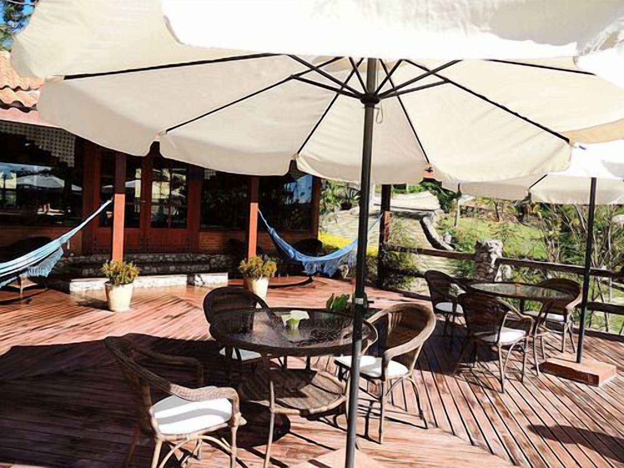 Un patio al aire libre con piso de madera, mesas, sillas y una sombrilla grande que proporciona sombra.