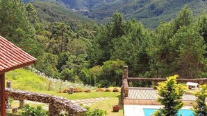 A view from a balcony with a stone railing, overlooking a lush valley with dense forest and distant mountains. - Pousada Cantinho das Estrelas (Camanducaia)
