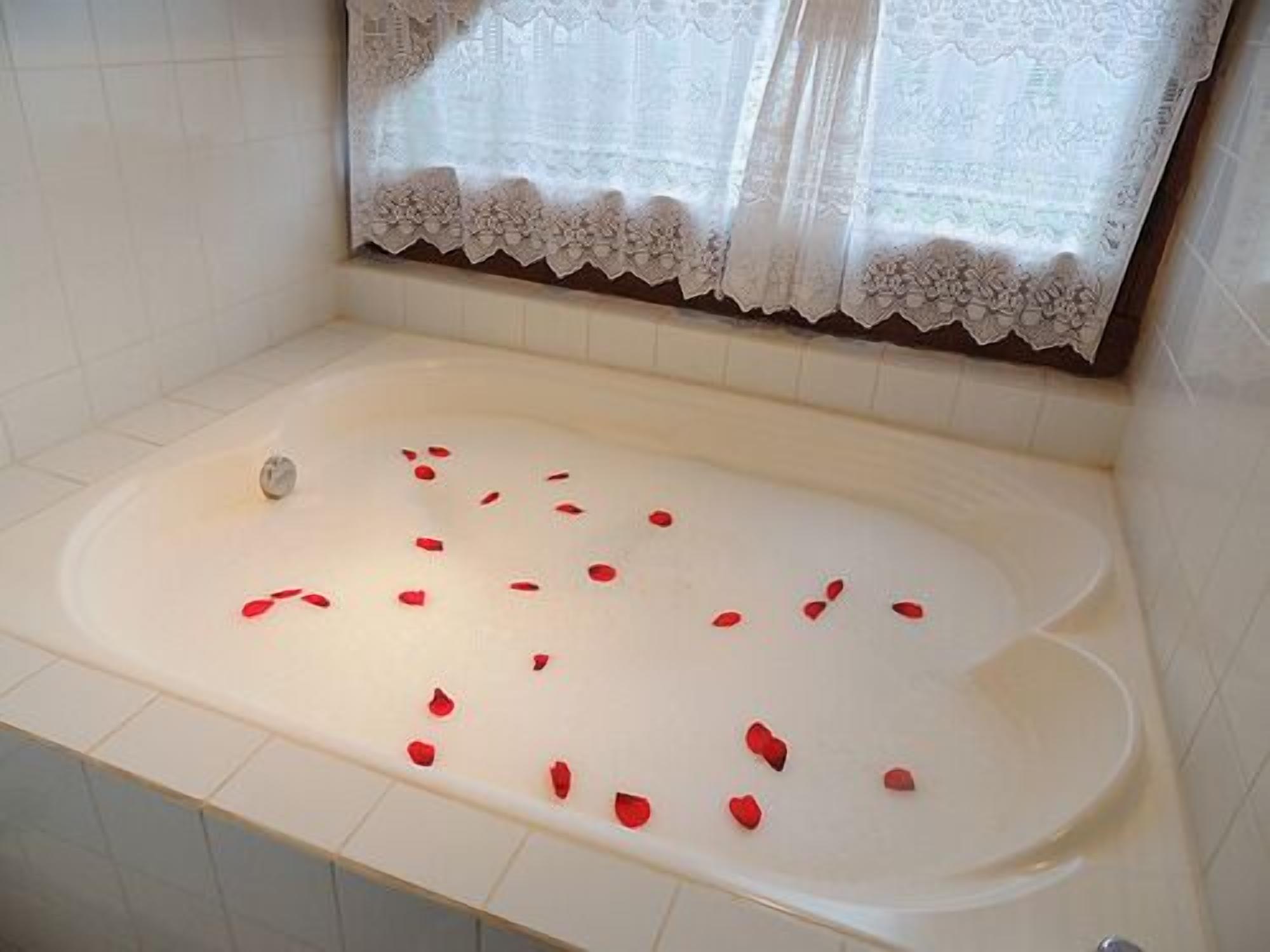 Un bagno con vasca, piastrelle bianche e una finestra con tende di pizzo.