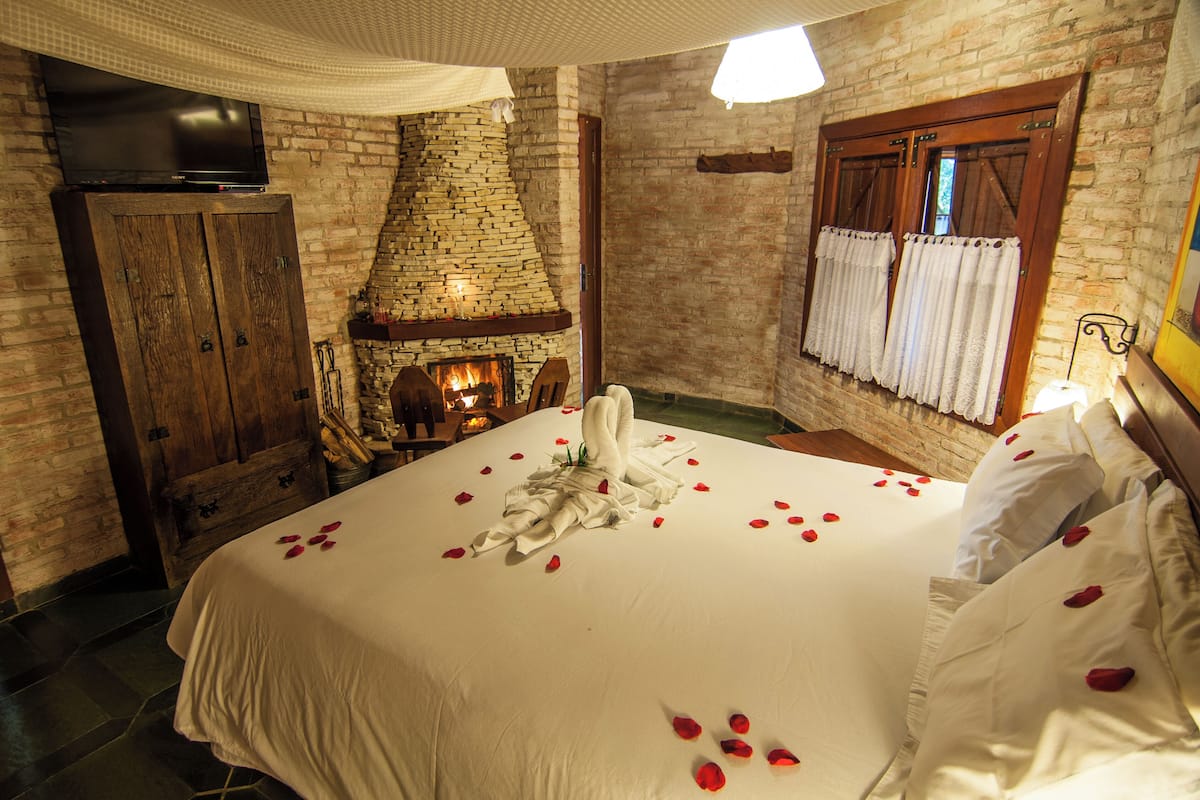 Ein Hotelzimmer mit Kamin aus Ziegelsteinen, einem Bett mit Rosenblättern und einem Holzschrank.