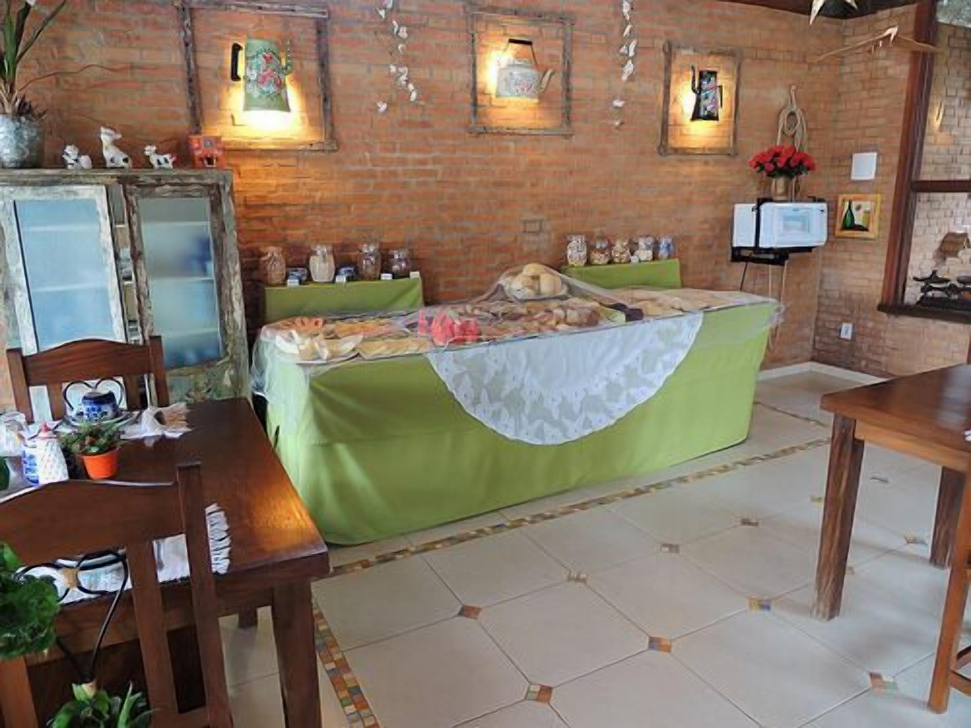 Um quarto com parede de tijolos, uma cama com colcha verde, uma mesa de madeira e uma cadeira.