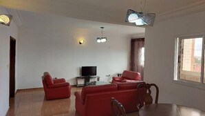 Un salon avec un téléviseur, deux canapés rouges, une table à manger et une fenêtre.